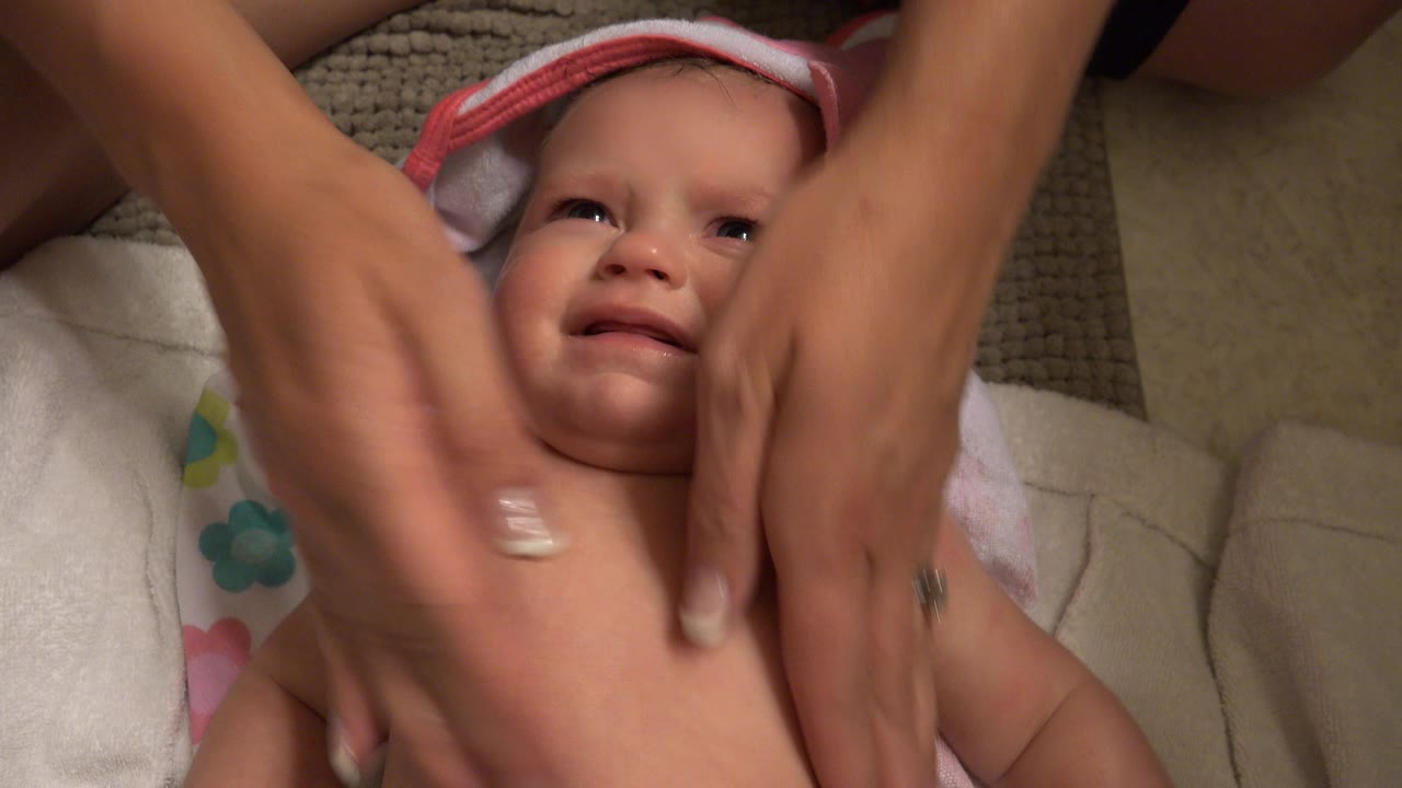 Adult hands massage a baby lying on towels.