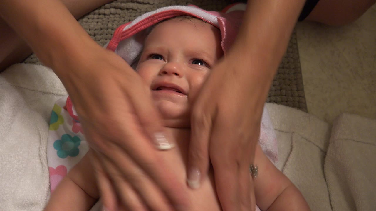In Westminster, Colorado, the caregiver's hands move across the baby's chest as the infant looks upward from towels and neutral household bedding.