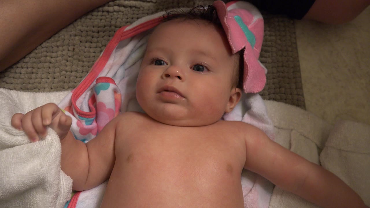 Baby lying on a white towel and pink blanket indoors