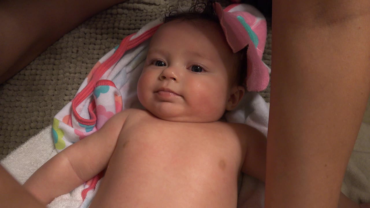 The baby remains centered on towels in a Westminster, Colorado home setting, with a cropped adult arm along the left side and soft light across the face and chest.