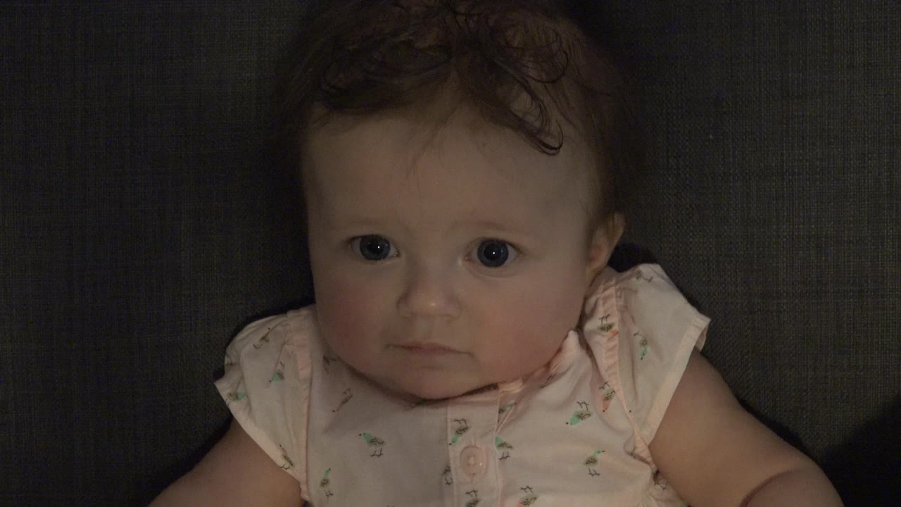 Baby facing camera with wide eyes on dark couch