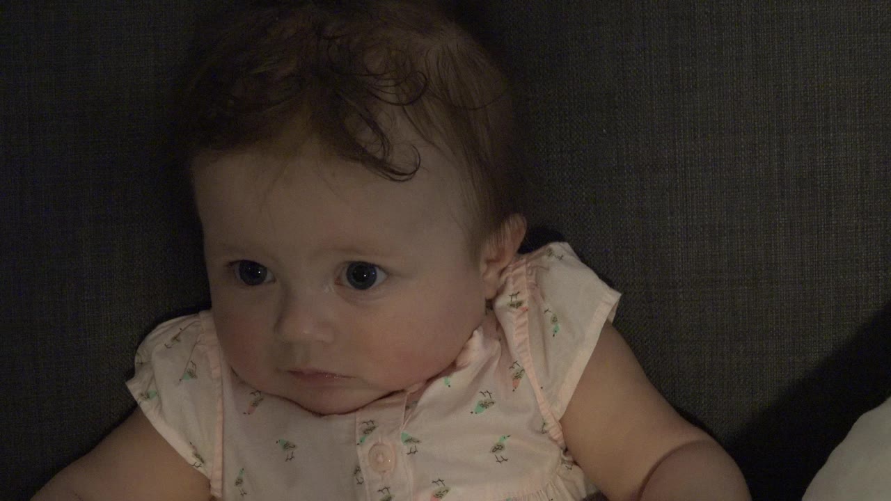 Baby girl sitting against a dark sofa and looking left.