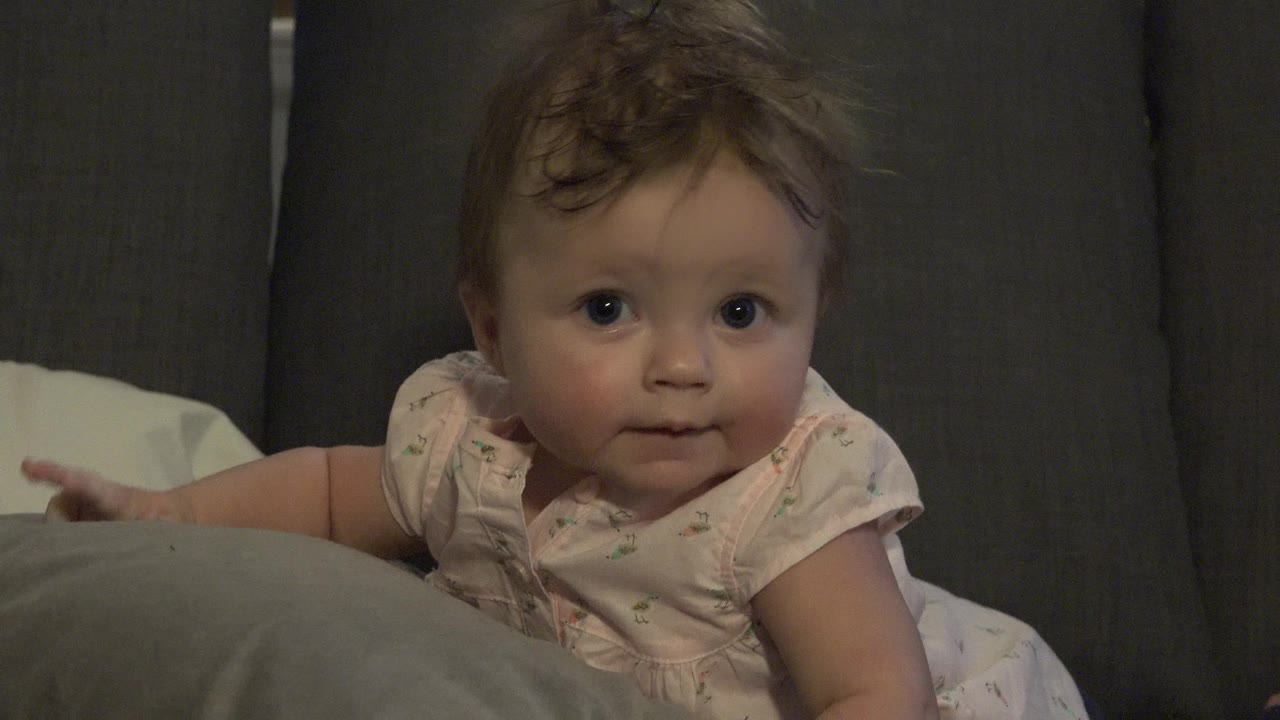 Toddler girl looking toward the camera on a gray couch.