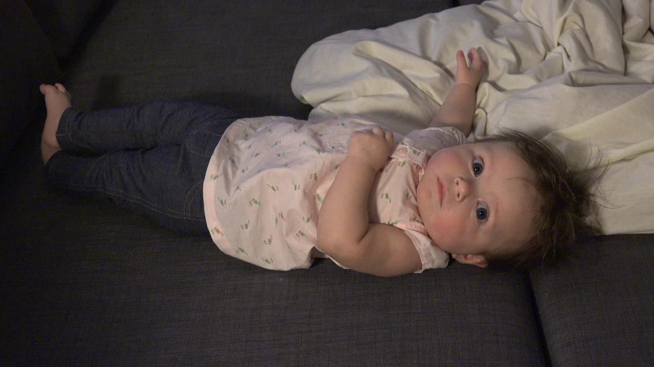 Baby lying on a dark couch beside a white blanket.