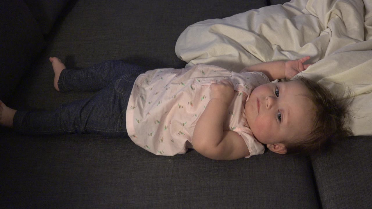 Baby lying on couch with head near a white blanket.