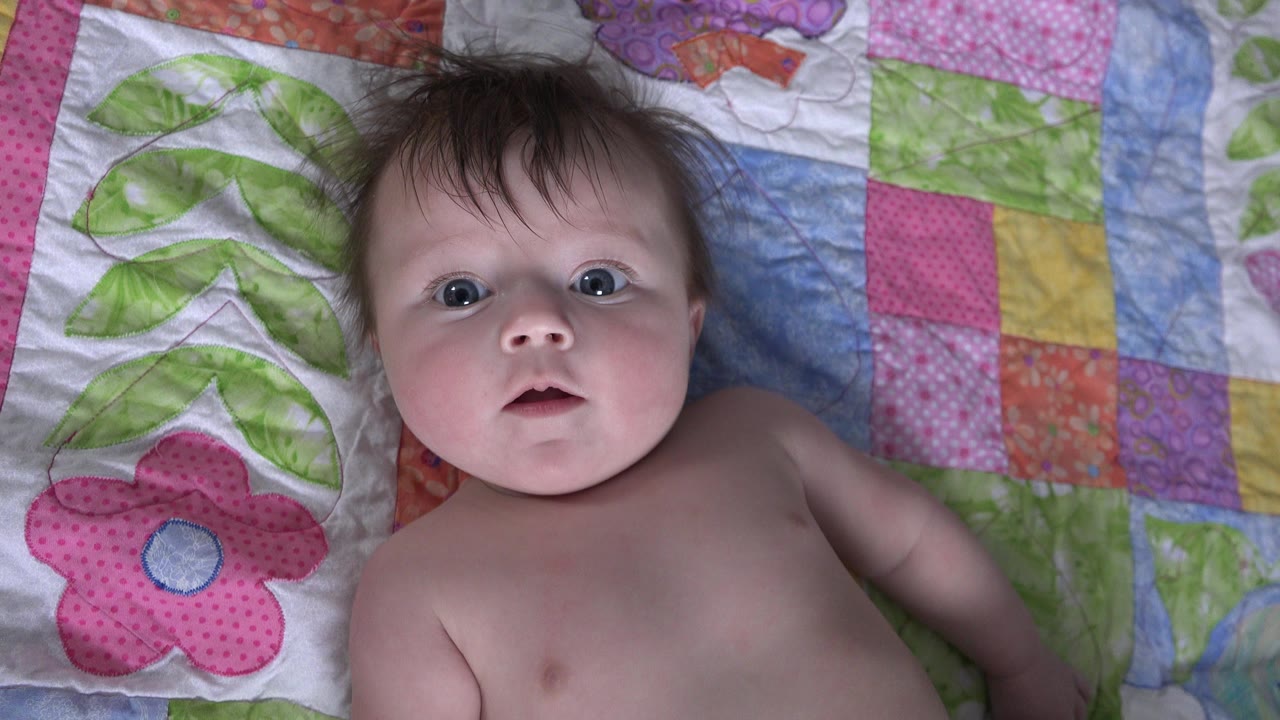 Baby lying on a colorful quilt and looking upward.
