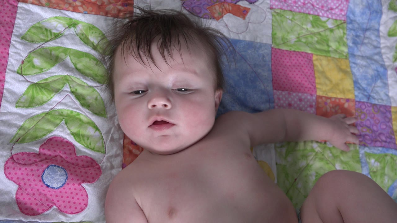 Infant lying on a pink and green quilt.