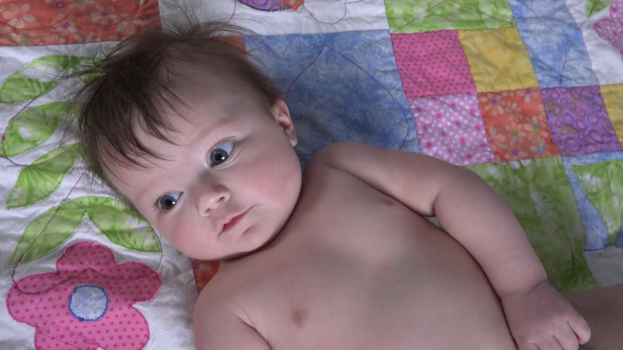 Infant girl lying on a colorful quilt and looking toward the camera.