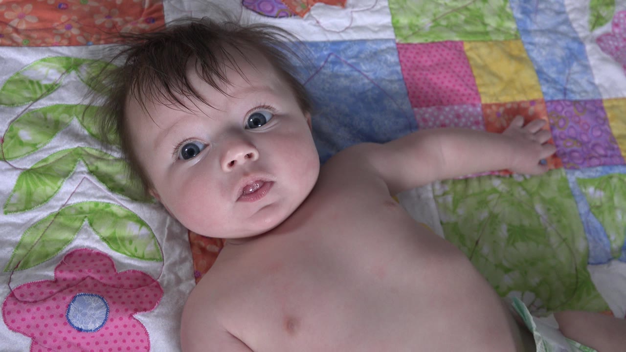 Baby lying on a colorful patchwork blanket looking toward camera.