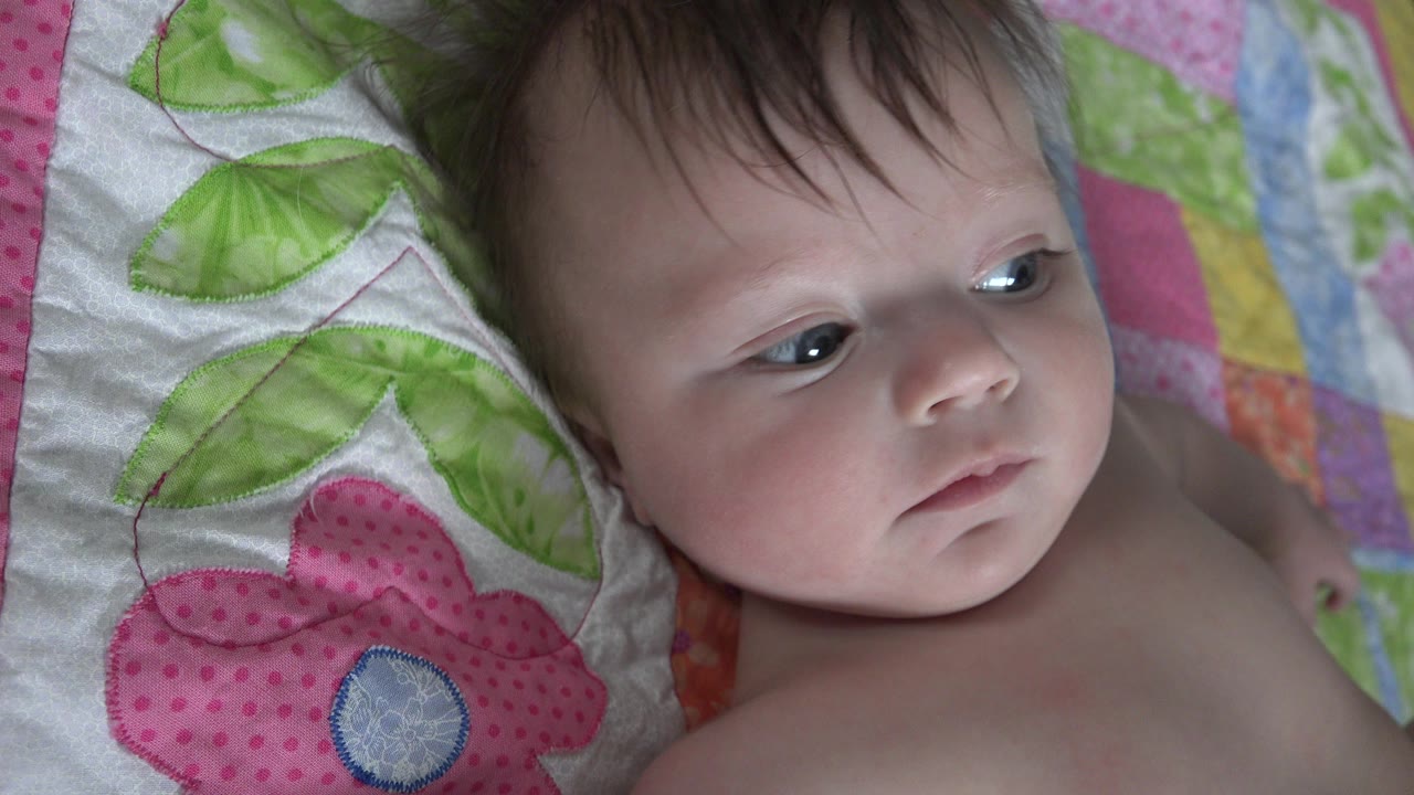 Baby lying on a colorful quilt and looking to the side.