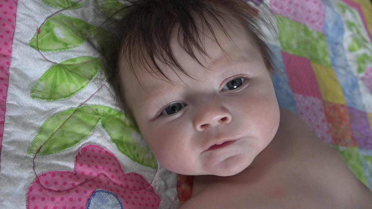 Infant lying on a colorful quilt and looking toward the camera.