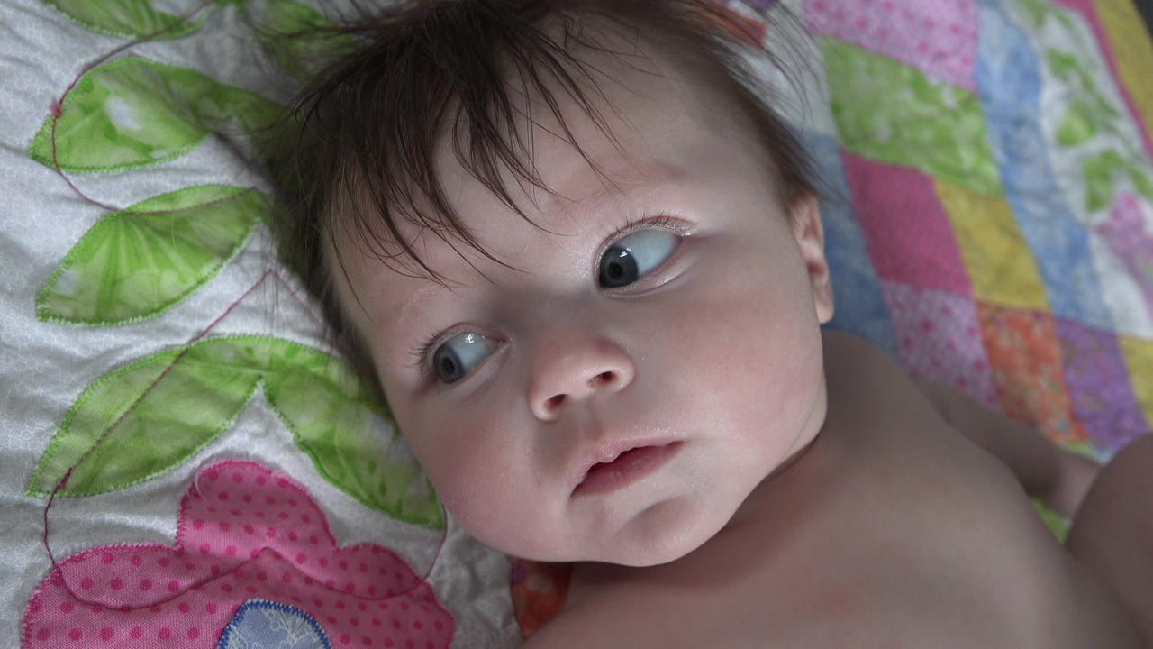 Infant on quilt looking sideways with face near center.