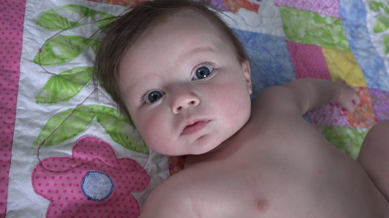Infant lying on a colorful quilt and looking toward the camera.