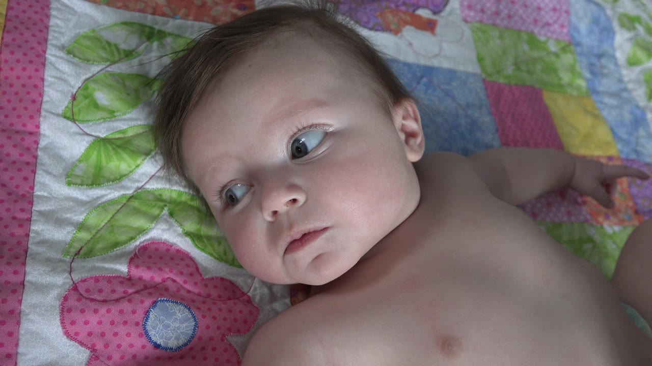 Baby lying on a colorful flower quilt and looking to the side.