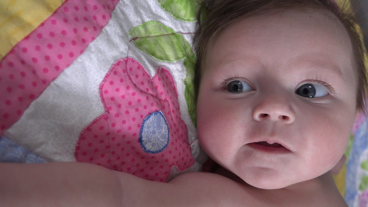 Baby lying on patterned bedding and looking off to the side.