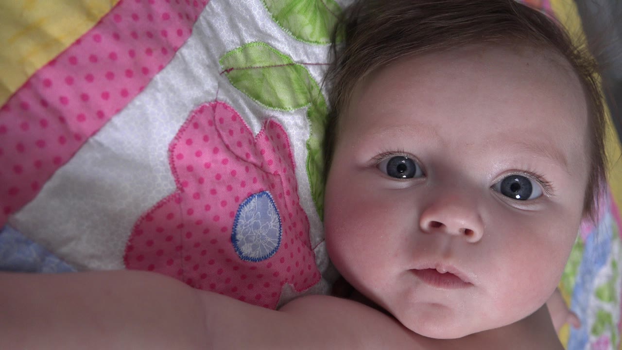 Baby girl lying on a colorful patterned blanket.