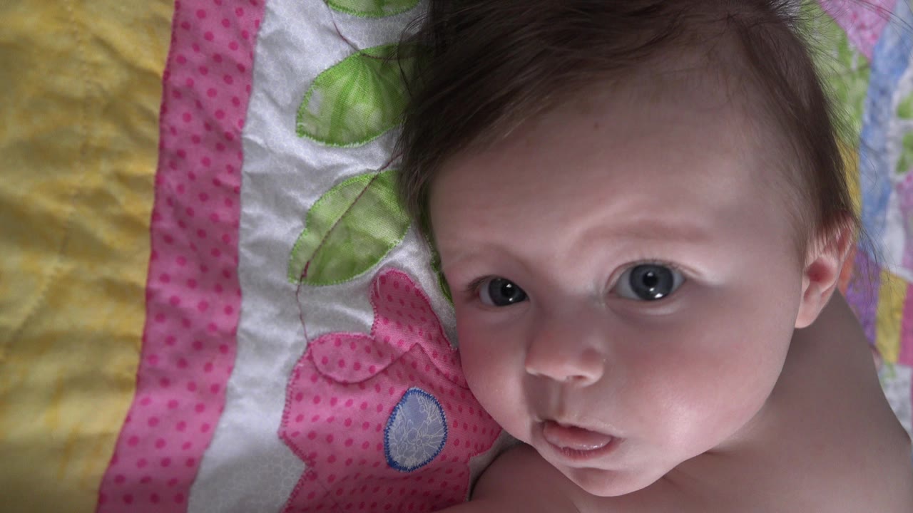 Baby boy lying on a colorful quilt and looking up at the camera.