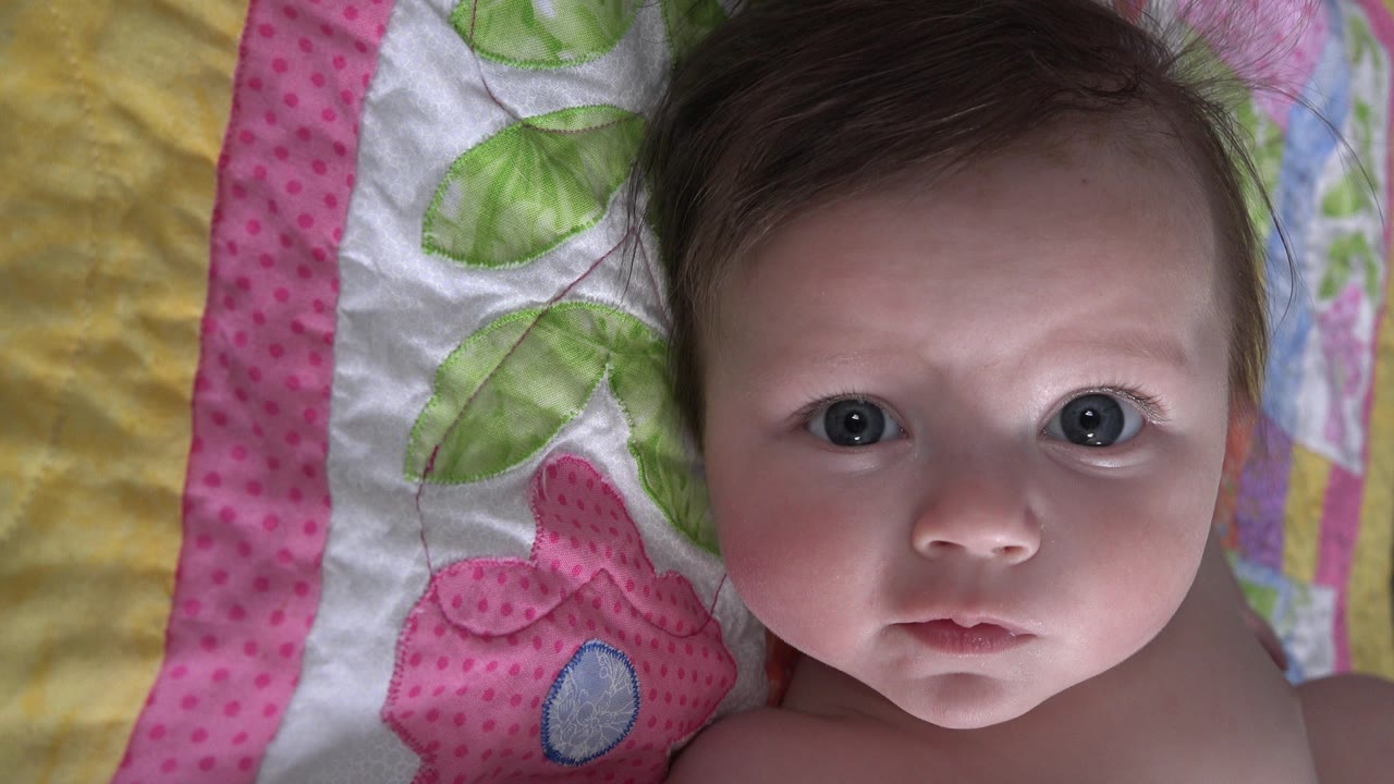 Baby facing upward on a pink and green quilt.