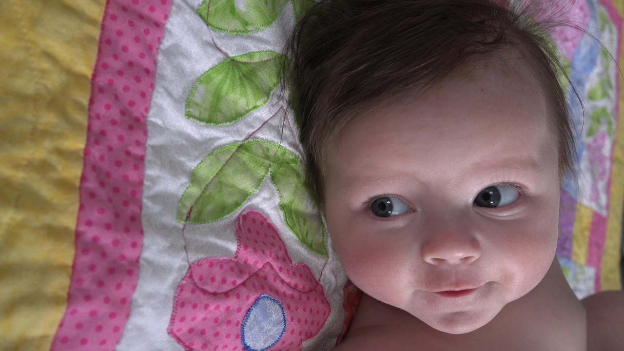 At 0:01, the infant remains on the colorful Westminster, Colorado blanket with her eyes turned sideways and her face softly lit from the front.