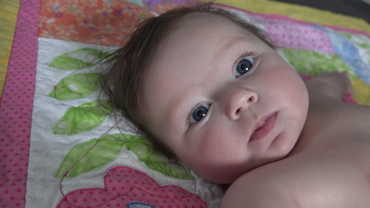 Baby lying on a colorful quilt and looking toward camera.