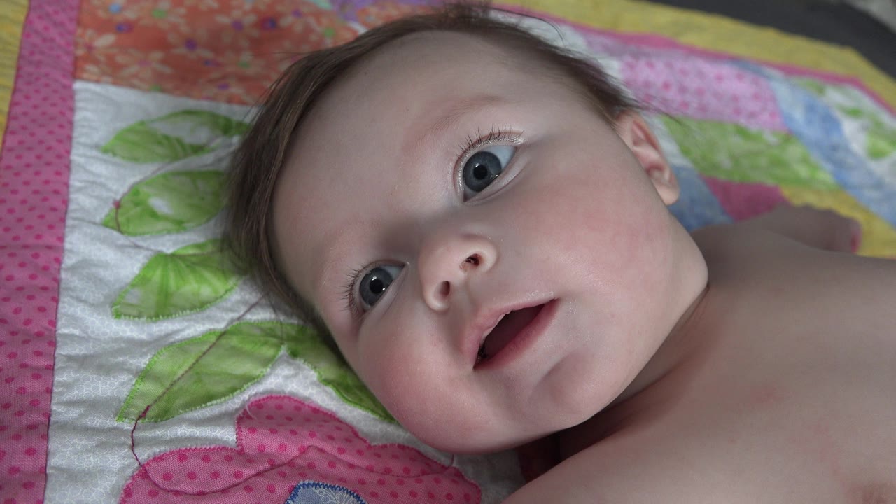 Blonde baby lying on a colorful quilt and looking up.