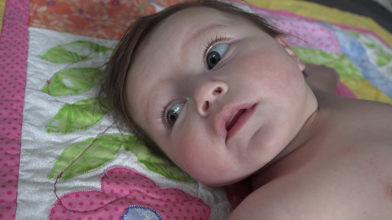 At 0:02, the infant lies on the same quilt in Westminster, Colorado, with the eyes turned to the side and the mouth slightly open.