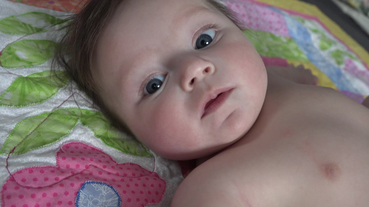 Baby lying on a colorful quilt and looking upward.