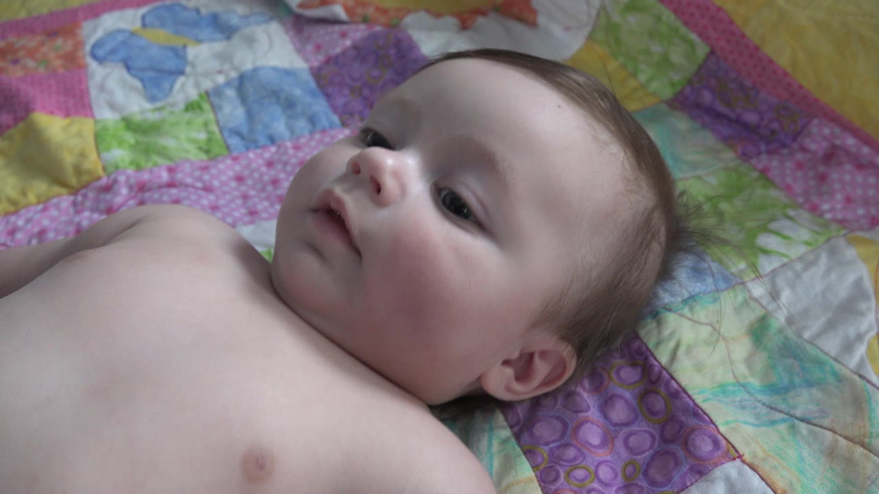Infant lying on a colorful quilt and looking upward.