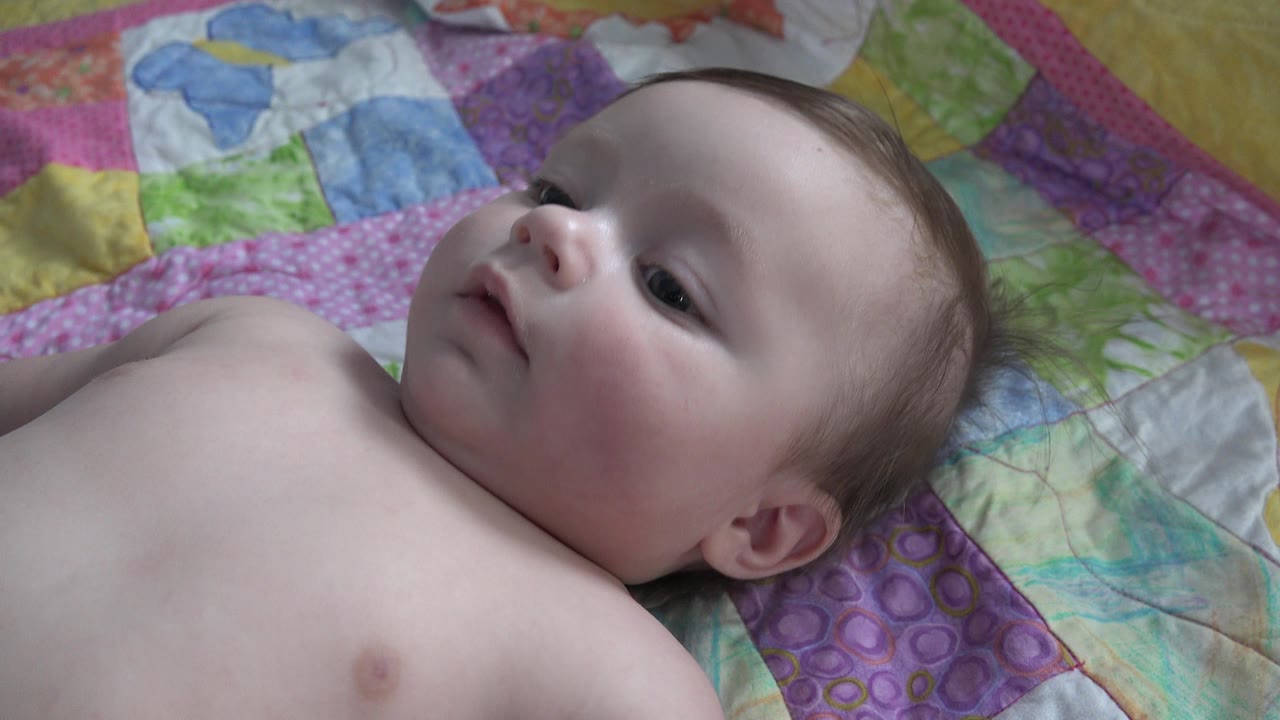 One second in, the infant remains on the colorful quilt in Westminster, Colorado, with eyes open and the head angled slightly toward the upper left of frame.