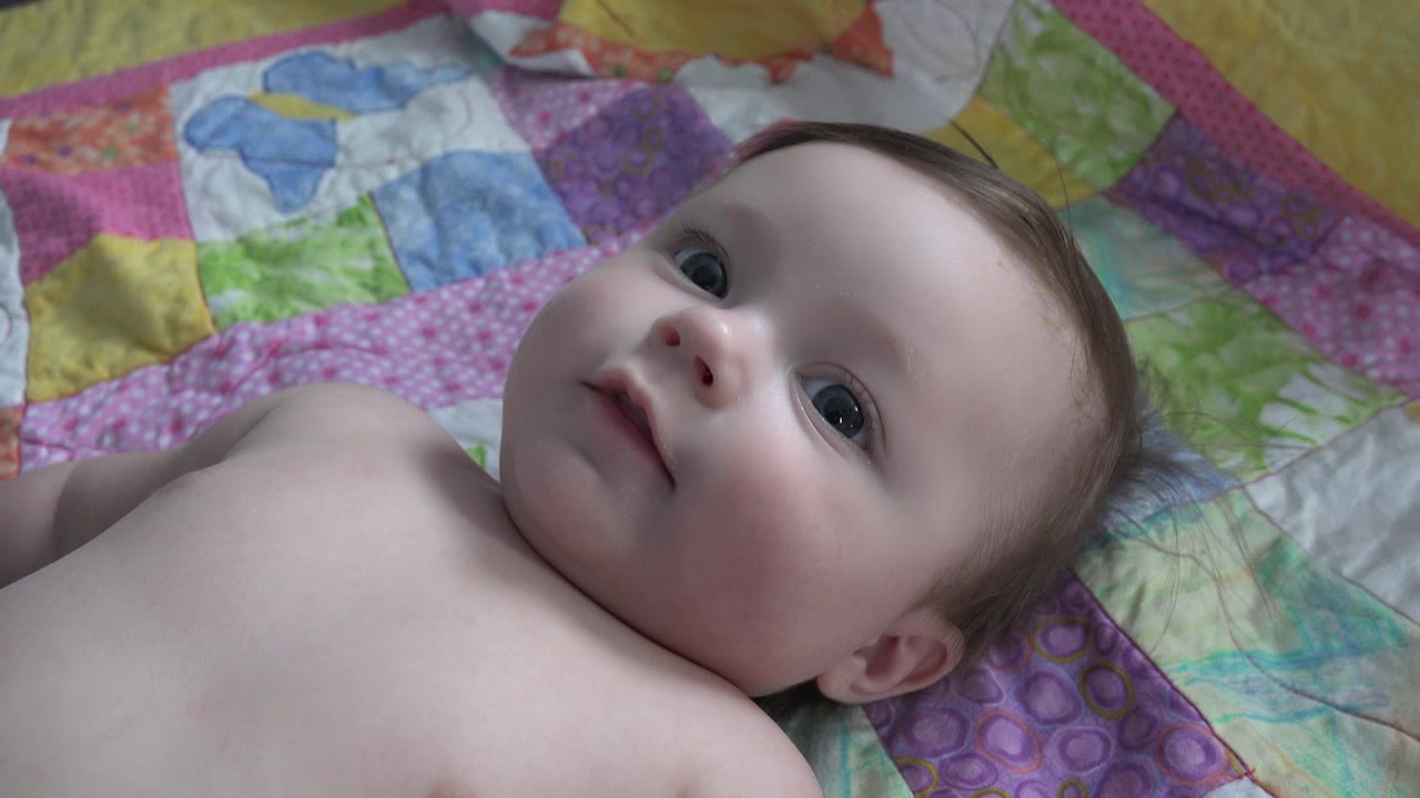 Infant lying on a colorful quilt and looking upward.