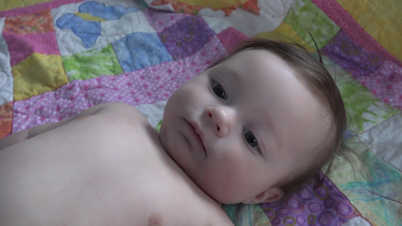 Baby lying on a colorful quilt and looking toward the camera.
