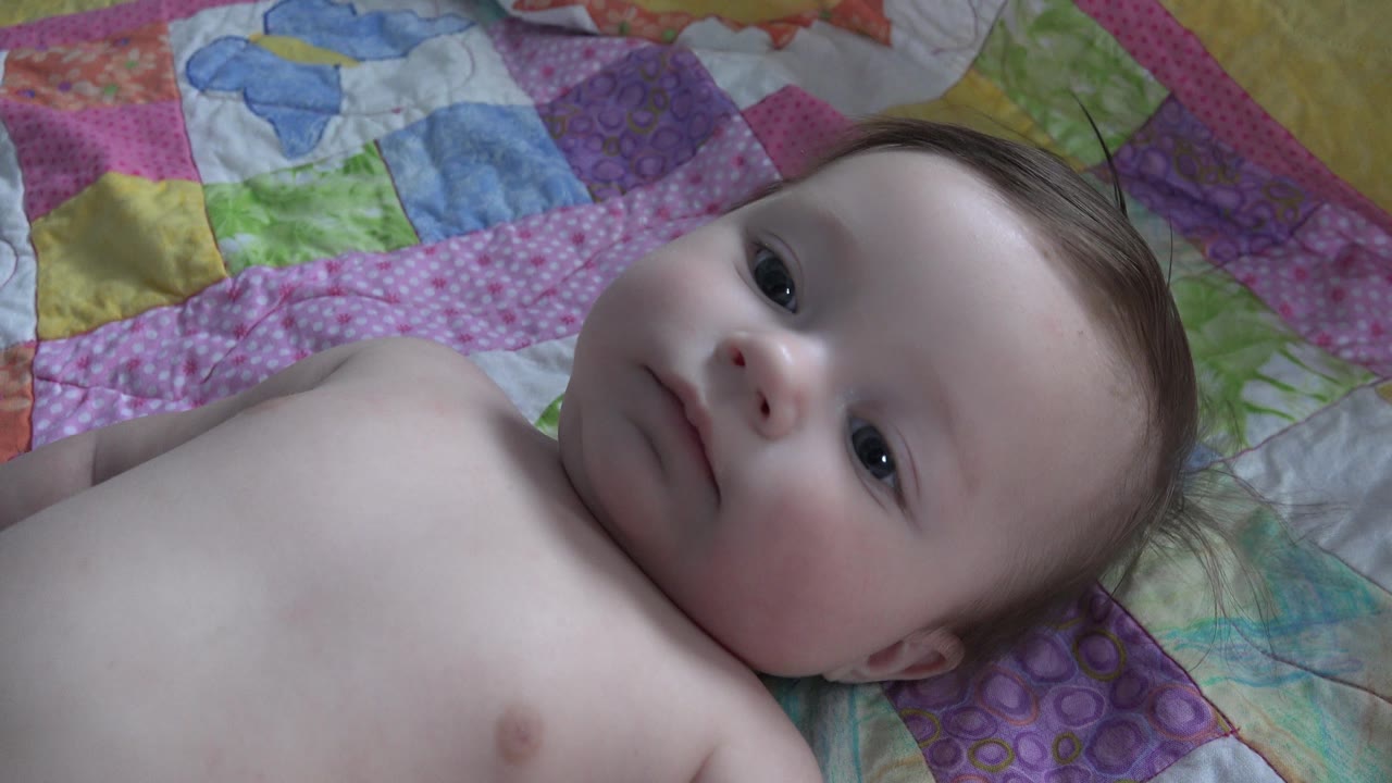 At 0:02, the baby lies on the patterned bedding in Westminster, Colorado, with more of the chest visible and the face turned slightly upward.