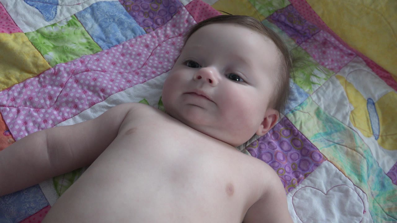 Infant lying on a colorful quilt and looking upward.