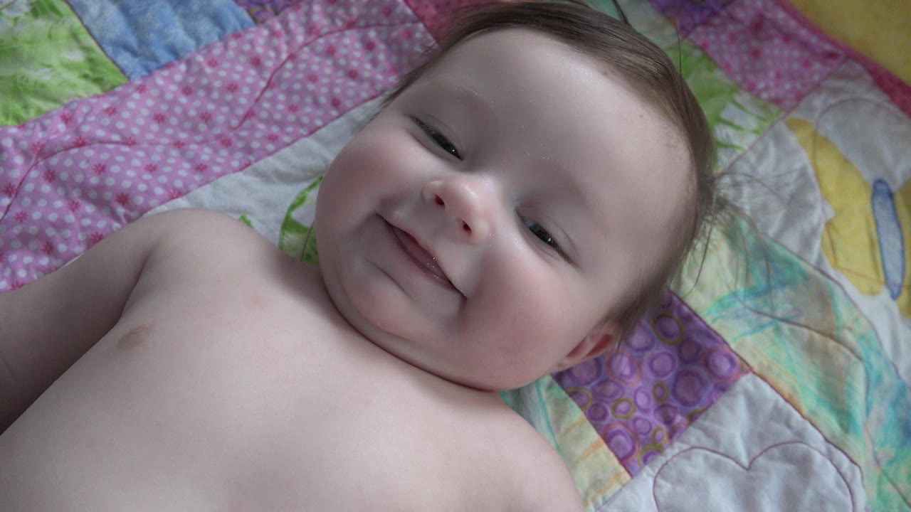 Baby smiling while lying on a colorful quilt.