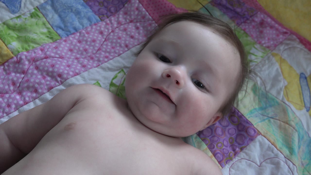 Baby looking toward camera on pink and purple quilt.