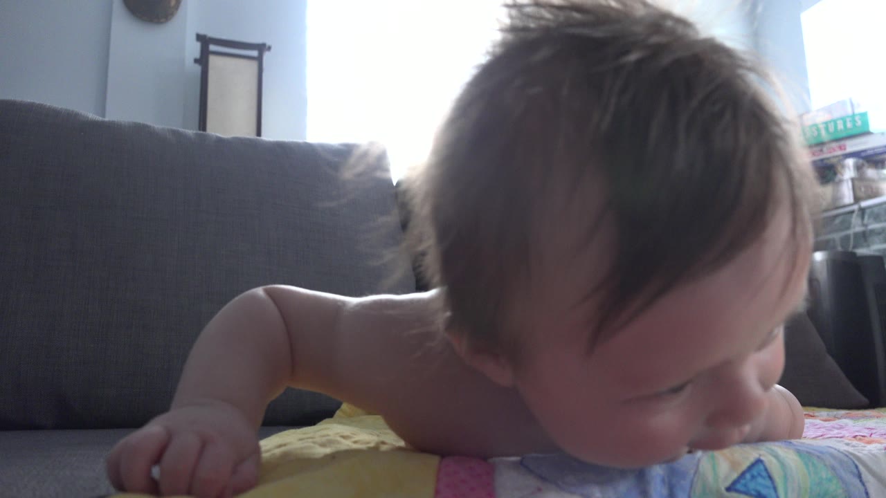 Infant lying belly down on a colorful blanket near a dark couch.
