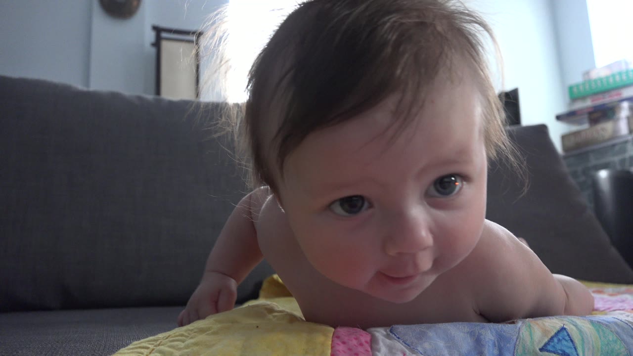 Baby on a colorful mat in front of a gray couch.