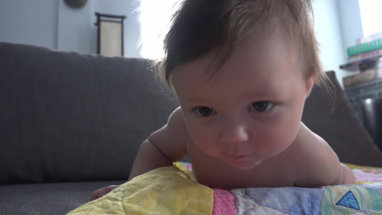 Baby lying on a colorful quilt near a gray couch.
