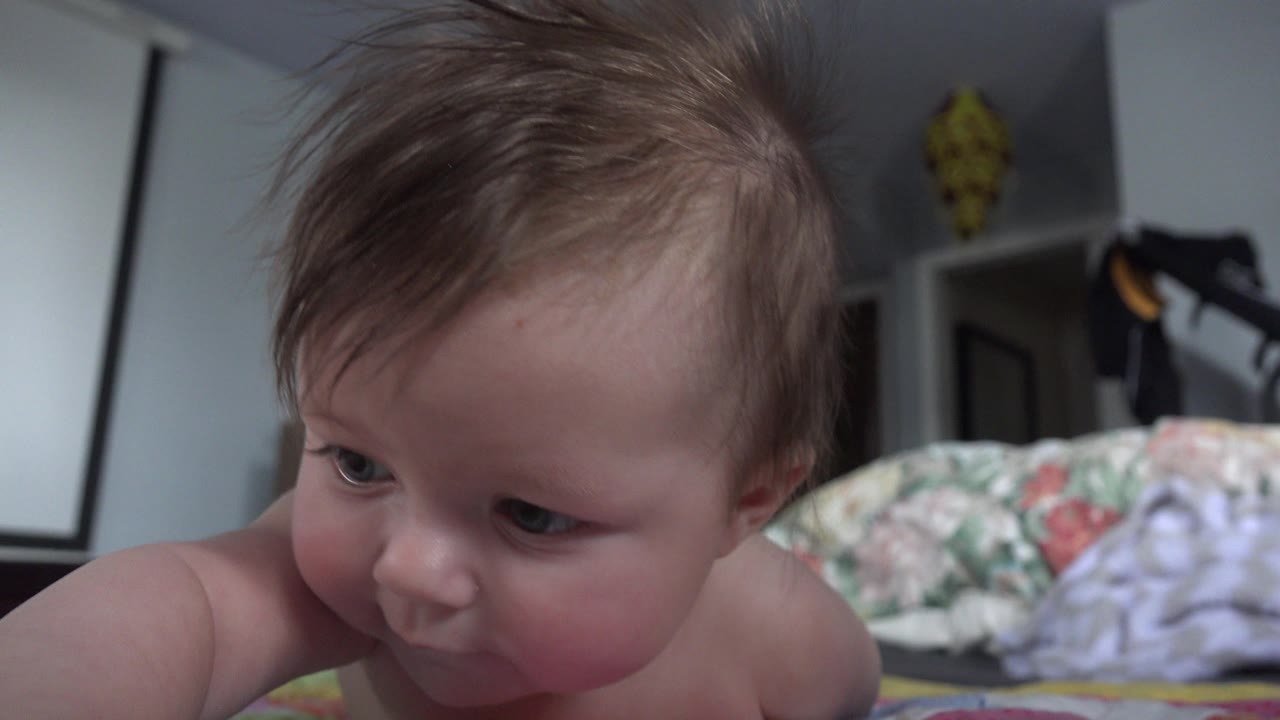 The baby remains close to the floor in the Westminster, Colorado home interior, with the face turned slightly downward and bedding blurred in the background.
