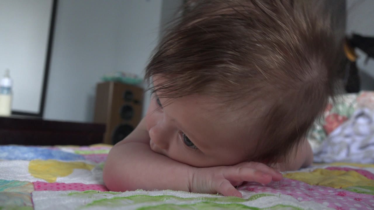 A baby in Westminster, Colorado rests face-down on a pink and green quilt, with the head turned left and a softly blurred bedroom behind.
