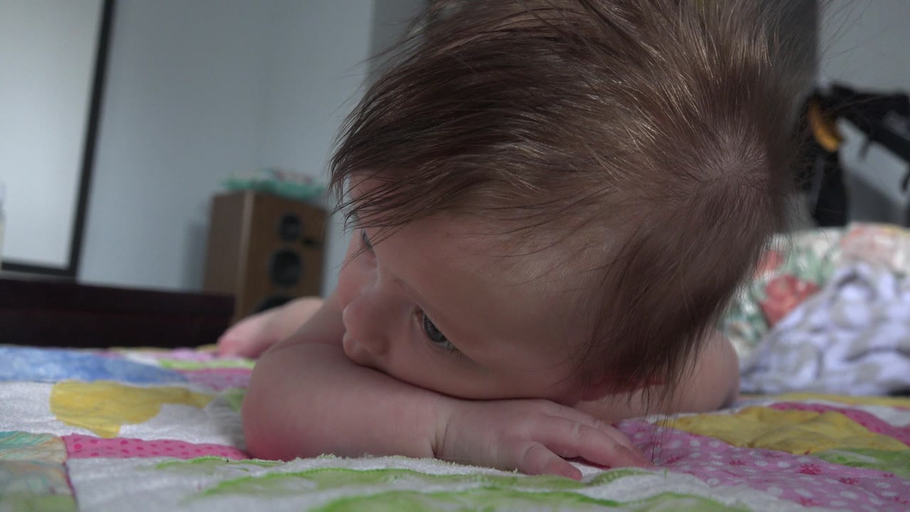 Baby lying on a quilt with one eye visible near the camera.