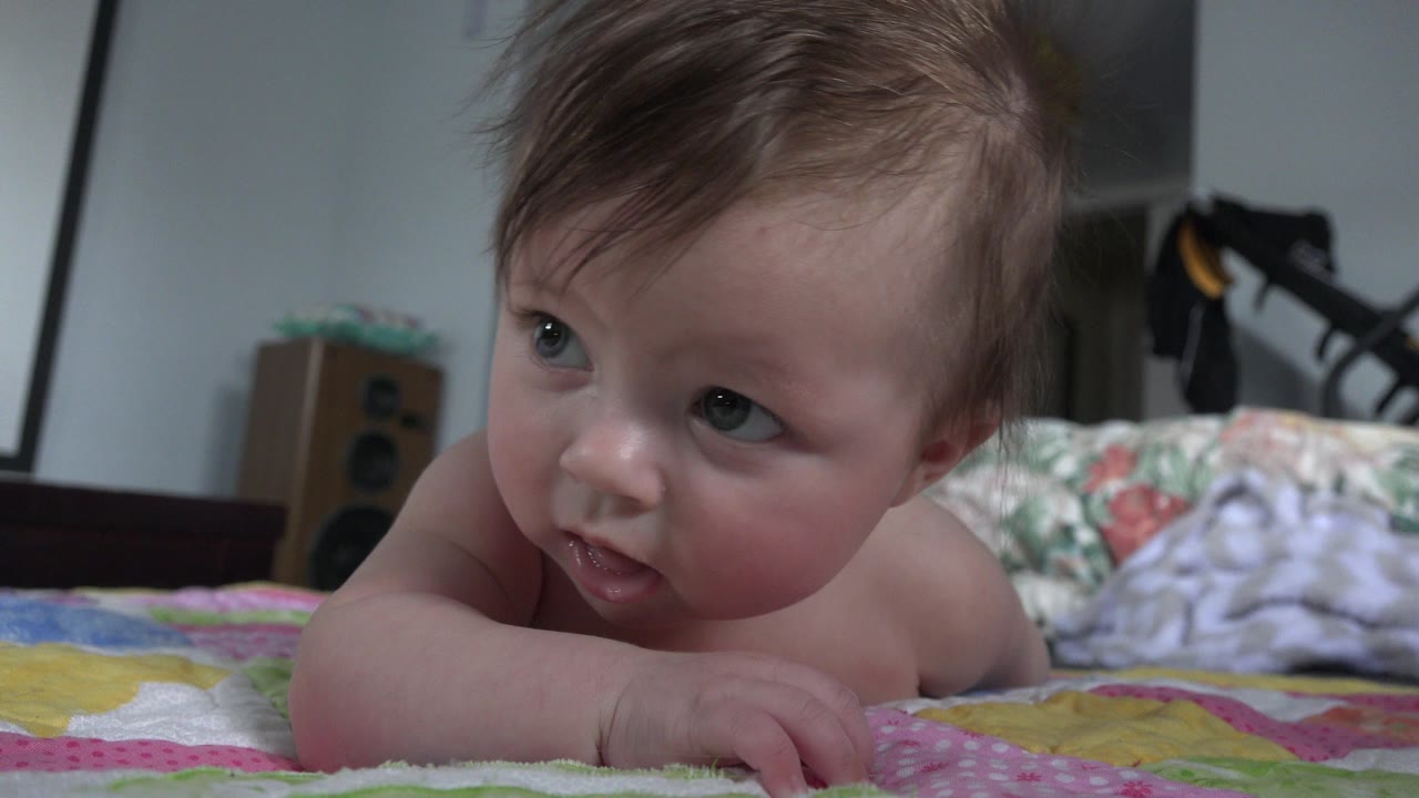 Baby on a colorful quilt looking off camera indoors.