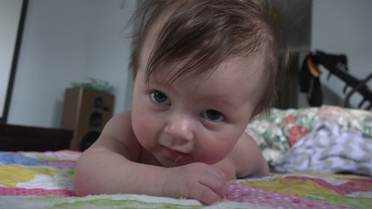Baby lying on a patterned blanket in a bedroom-like interior.