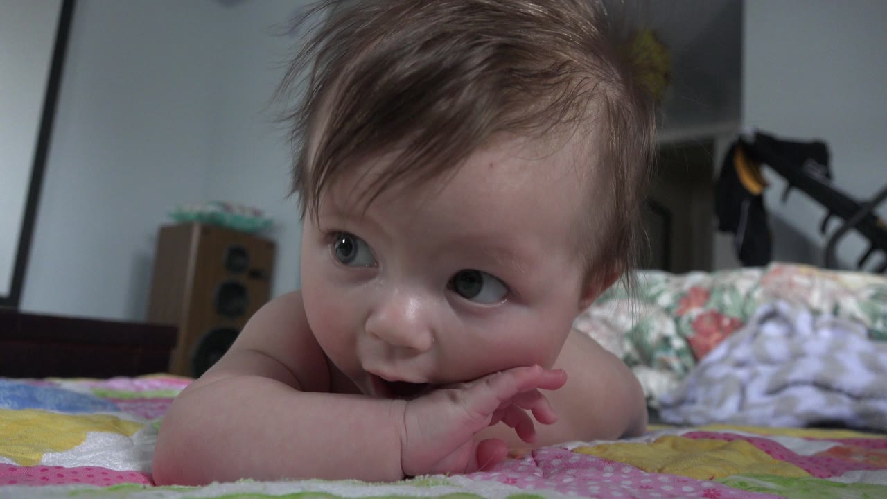 Baby lying on a quilt chewing one hand.