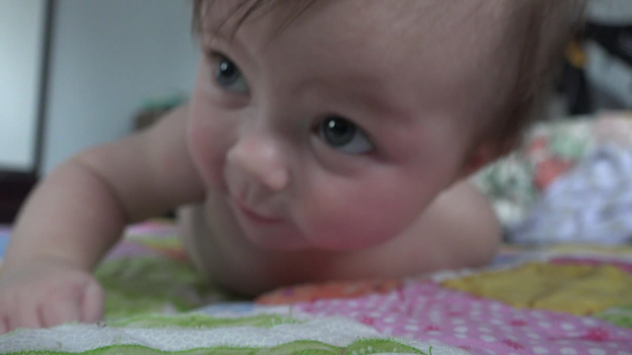 Baby lying on a patterned blanket and looking to the side.