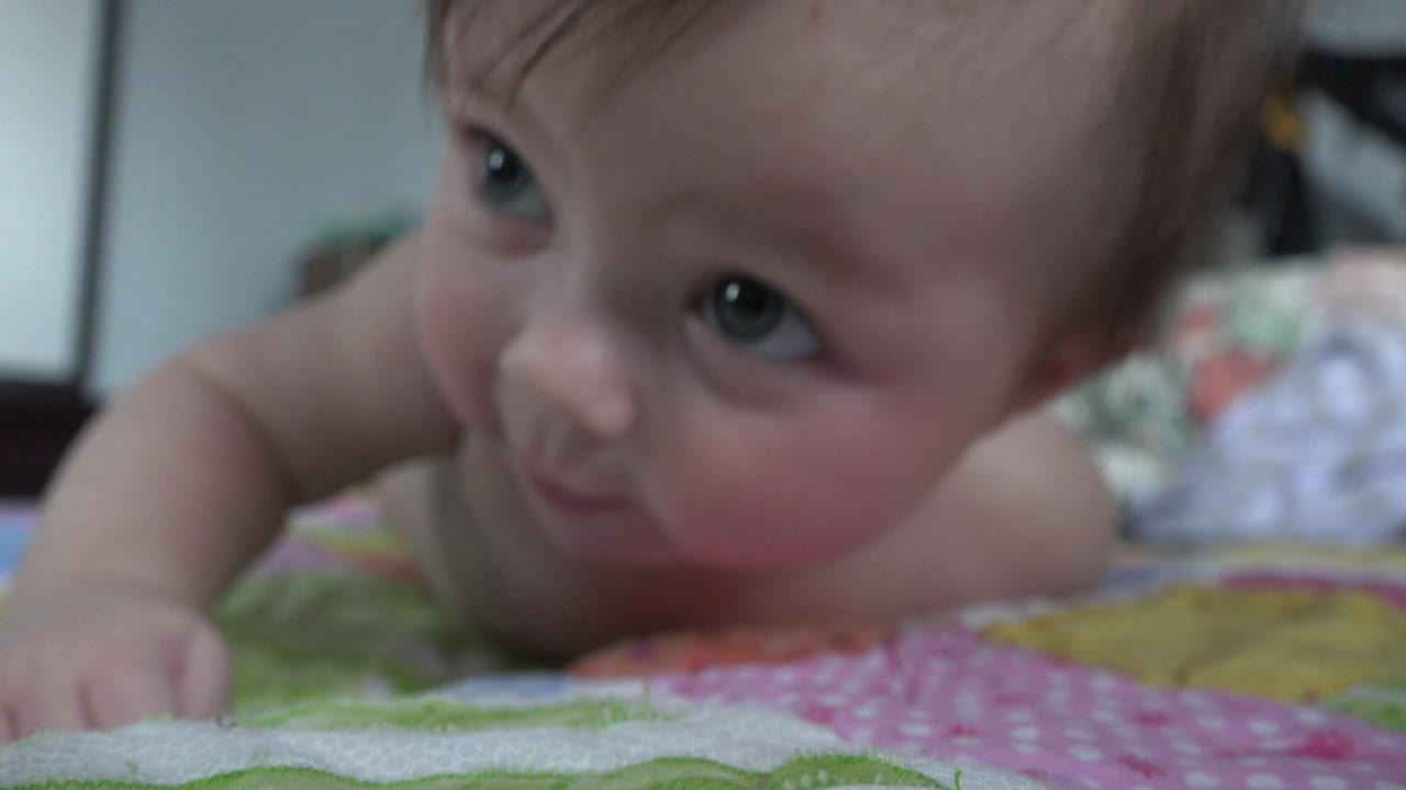At 0:01, the infant stays belly-down on the blanket, with the head lifted slightly and eyes glancing upward in the Westminster, Colorado home-video frame.