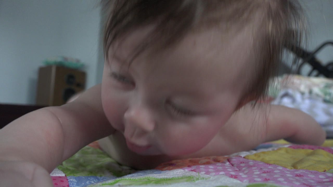 Baby lying face down on a colorful bed with eyes closed.