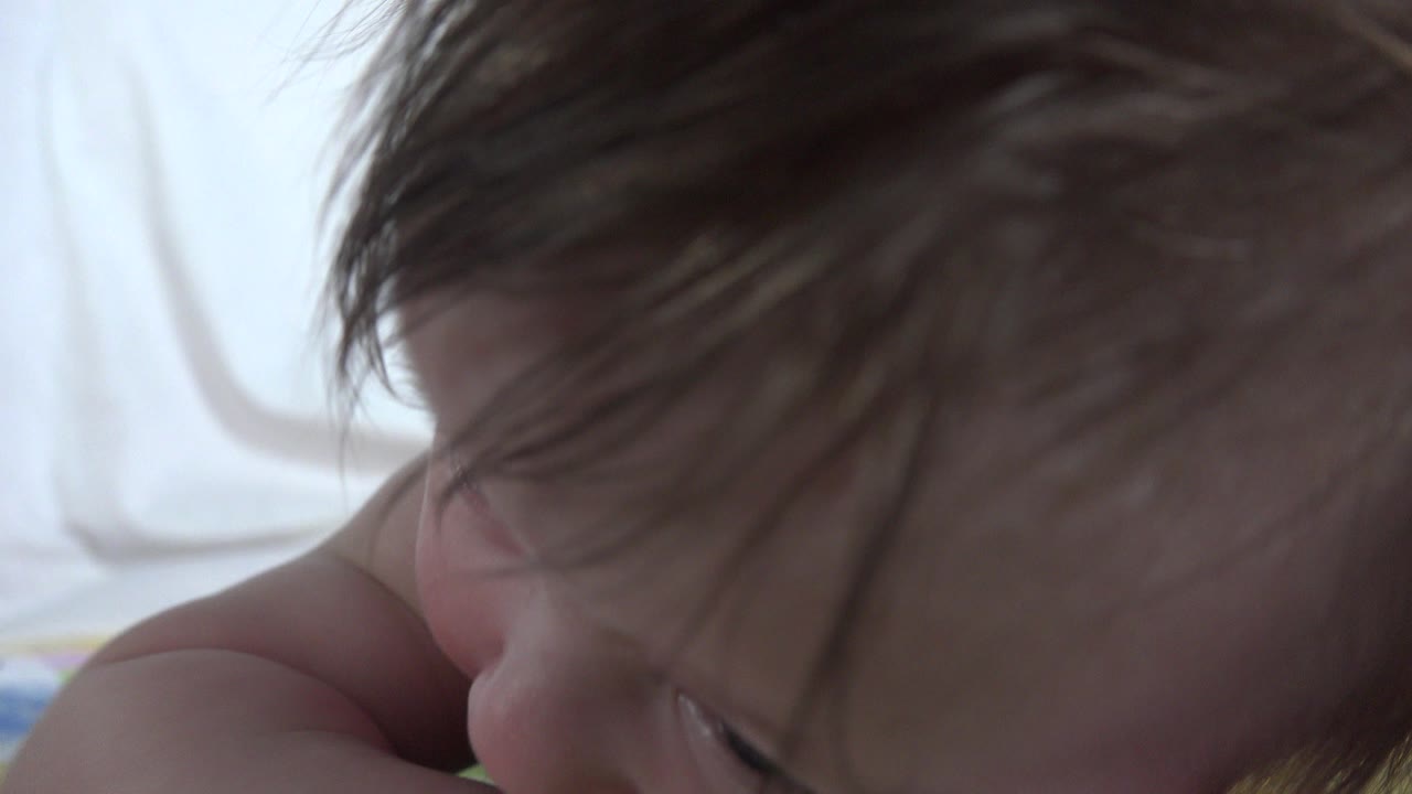 Close-up of an infant in Westminster, Colorado lying on a soft surface, with brown hair covering much of the forehead and one eye partly visible near the bottom of the frame.