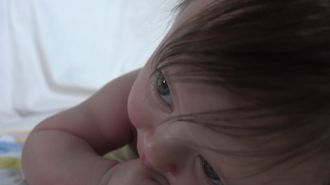 Baby looks toward the camera from a bed in close-up.