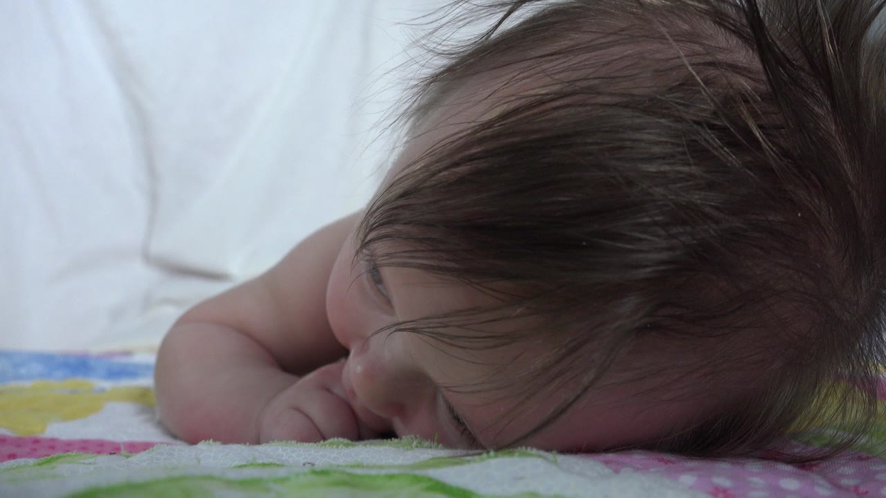 Baby lying face down on a colorful quilt beside a white pillow.